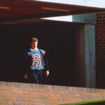 a student wearing a blue shirt with a red 'S' on the front leaving the library entrance.