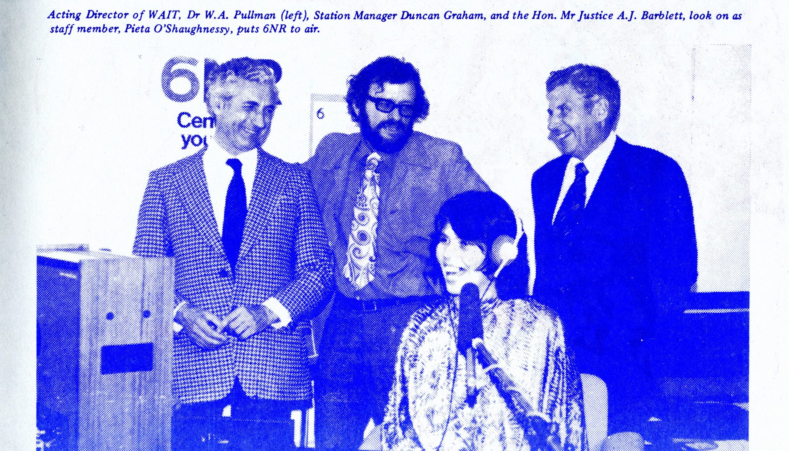 Blue monotone image of 3 men in suits smiling behind a woman sitting at a microphone. Caption reads 
