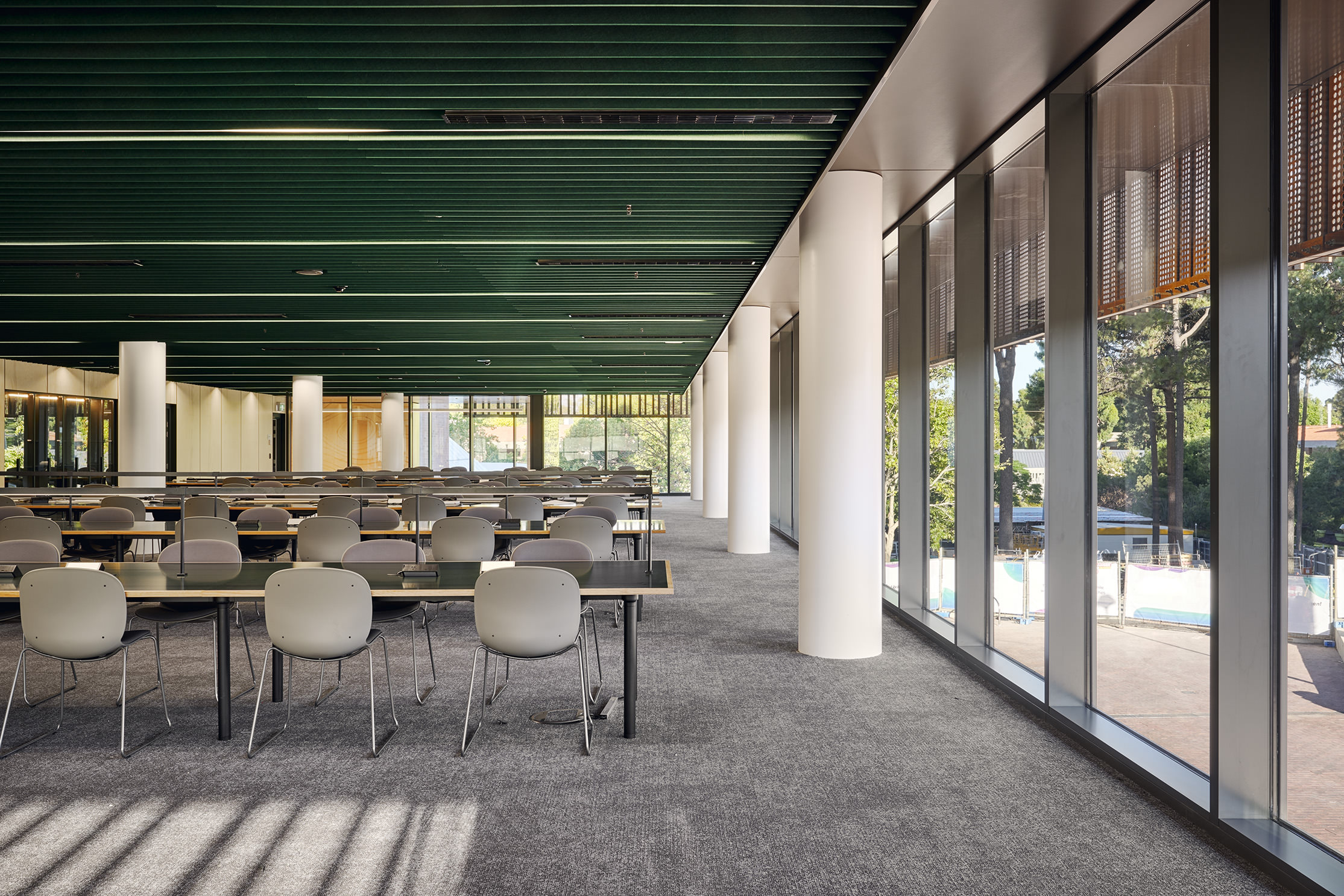 grey chairs and green desks in the bright library space. there are windows to the right.