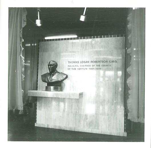 black and white photo of a statue bust on a ledge, with wall lettering "Thomas Logan Robertson C.M.G. Inaugural chairman of the council of this institute 1967-1969"
