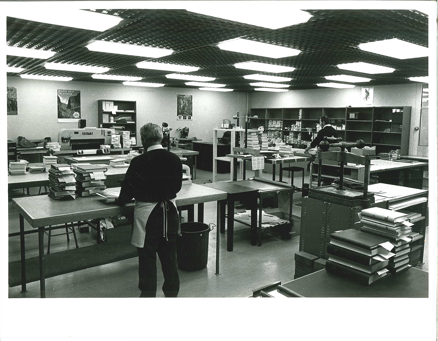 black and white photo of large warehouse room with tables, books and workers